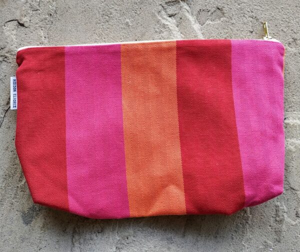 makeup bag red orange pink flat on the floor with a stone grey background