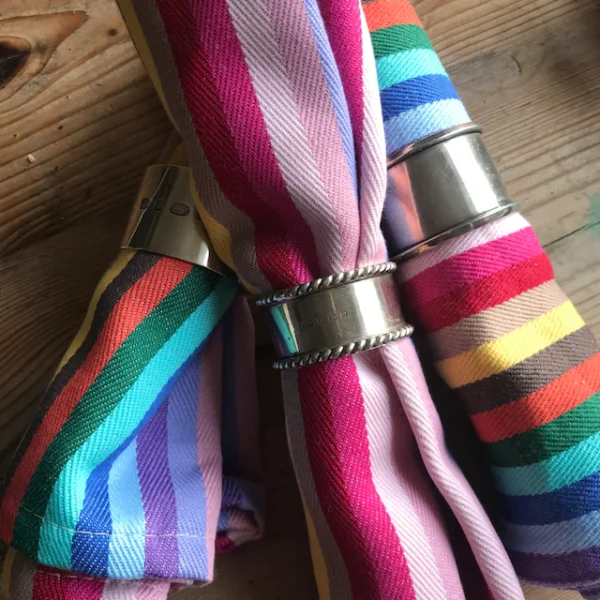 3 rainbow napkins on a wooden table individually rolled in silver rings